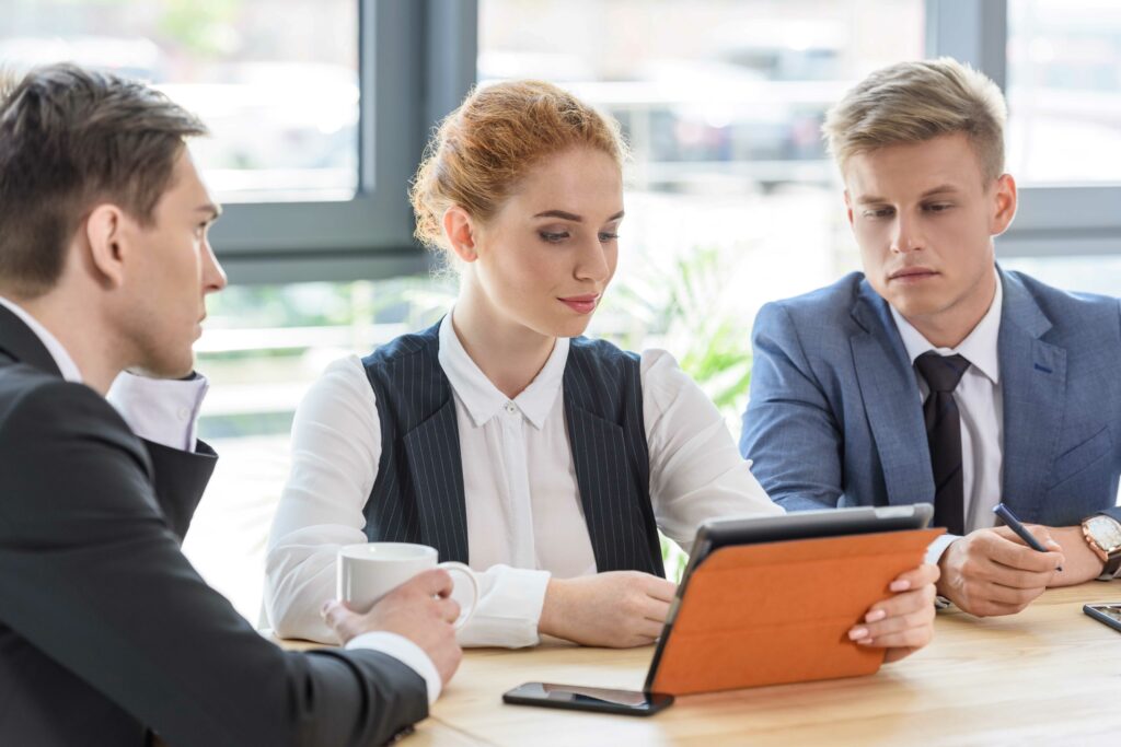 Three people in a project meeting viewing a tablet. Source: DepositPhotos.com